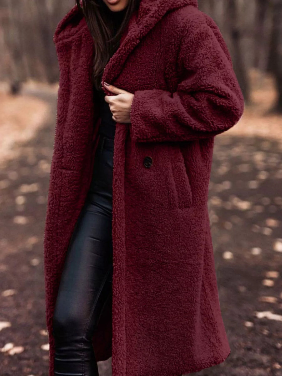 Longline teddy bear coat in wine red with hood and button closure, styled with black pants.