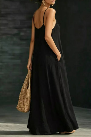 Black a-line maxi dress with spaghetti straps and pockets, held by a model with a straw bag.