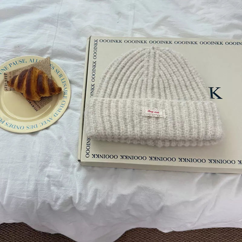 Cozy chunky knit beanie hat in Milky White with a decorative tag.