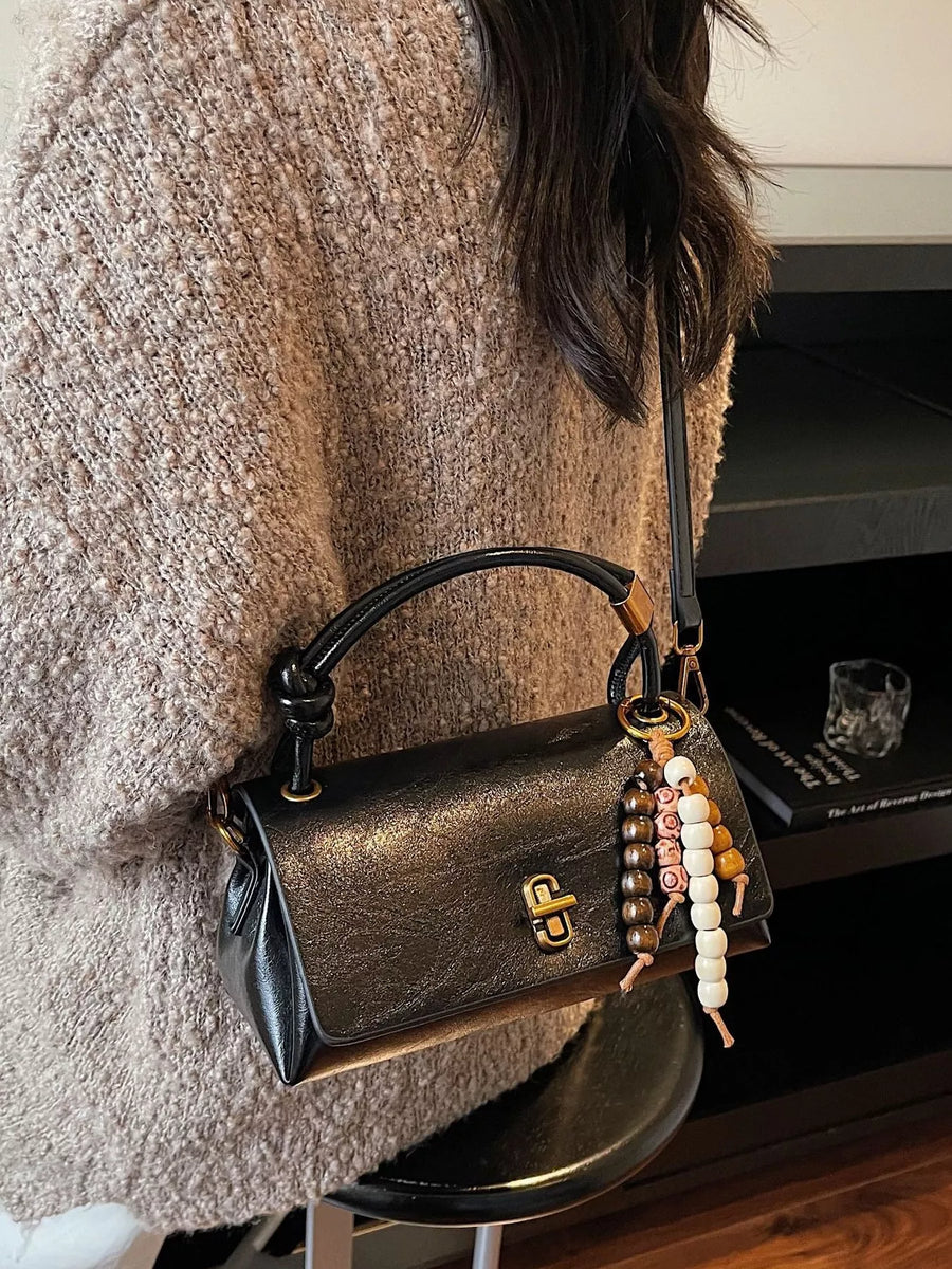Black leather crossbody bag with beaded charm detail and knotted handle.