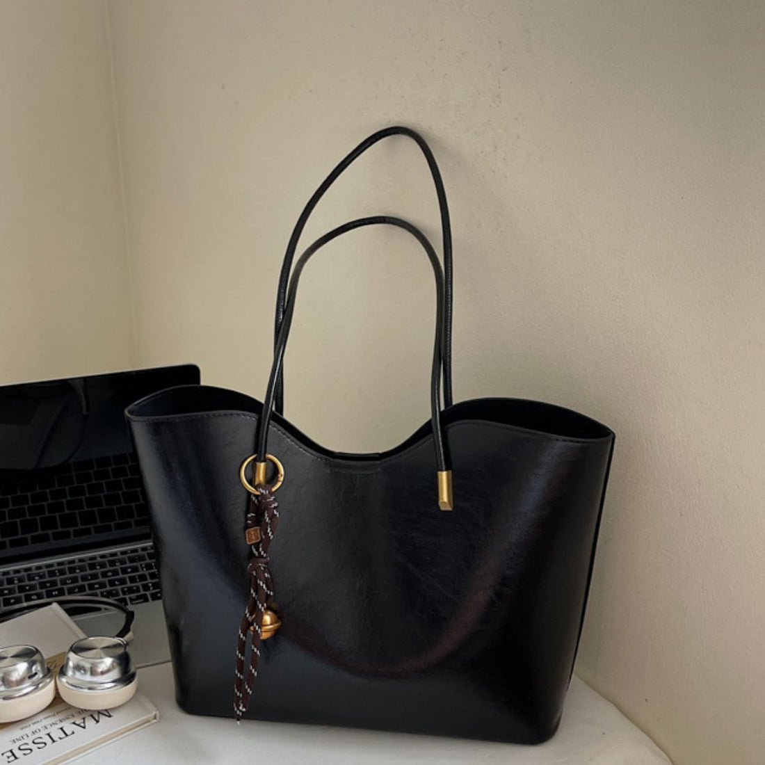 Black pu leather large tote bag with decorative tassel and bell charm.