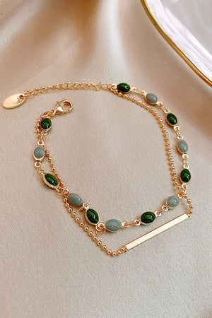 Dual chain gold bracelet with green and grey oval stones and a gold bar accent.
