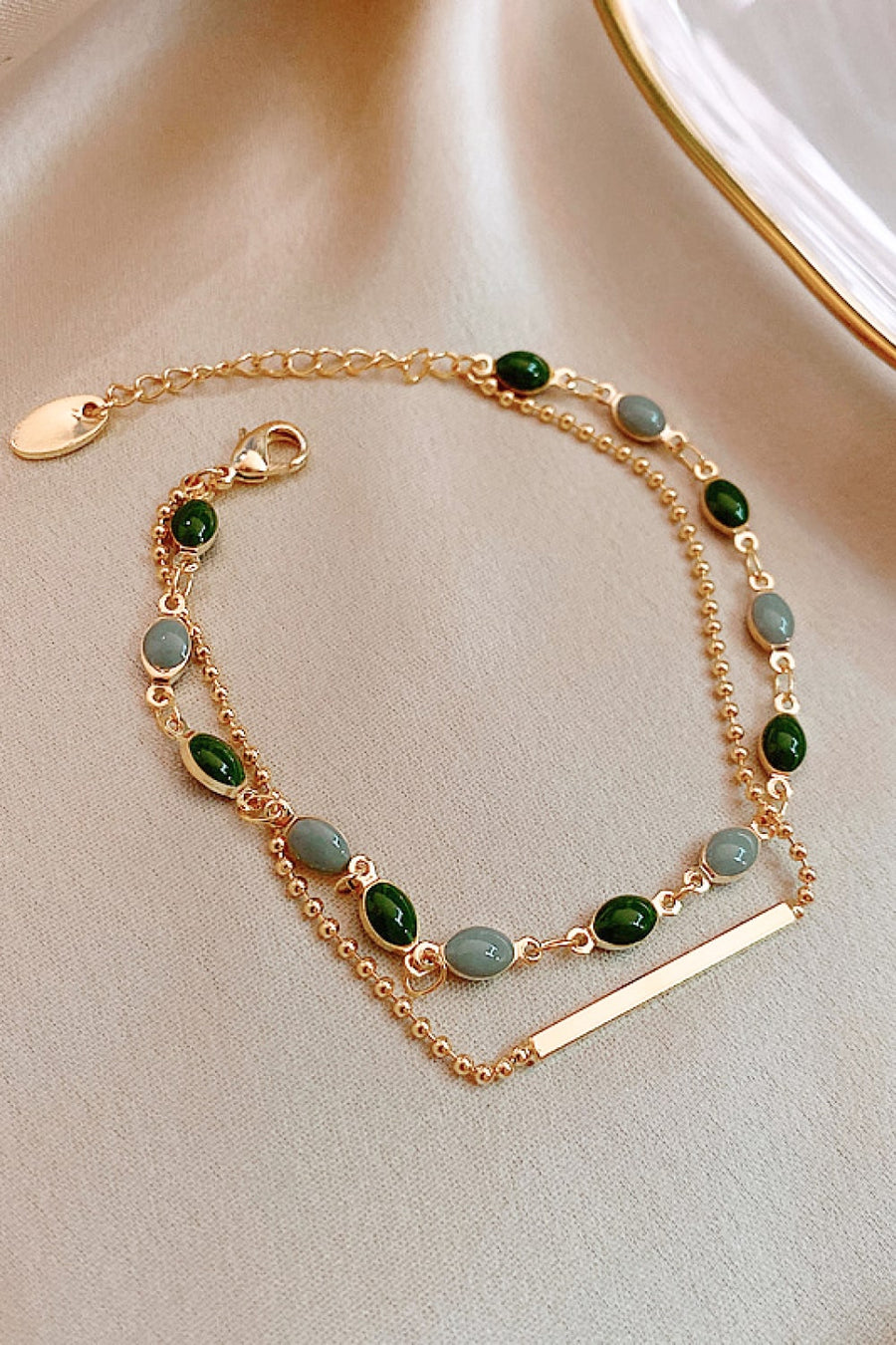 Dual chain gold bracelet with green and grey oval stones and a gold bar accent.