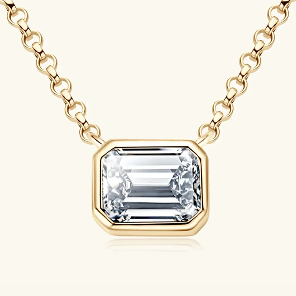 Gold bezel necklace with emerald cut moissanite pendant on a link chain.