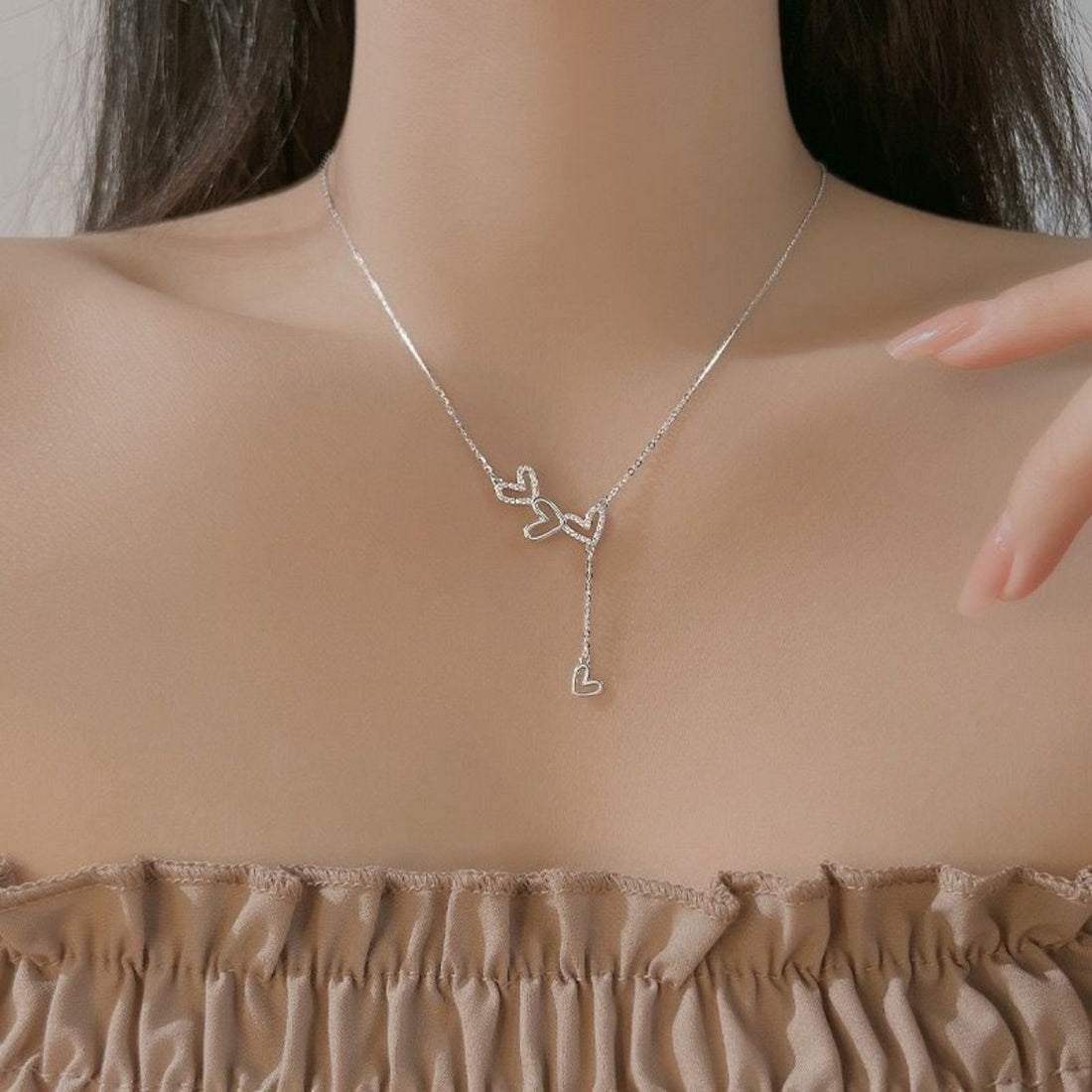 Sterling silver Y-necklace with delicate heart charms, resting on the collarbone.