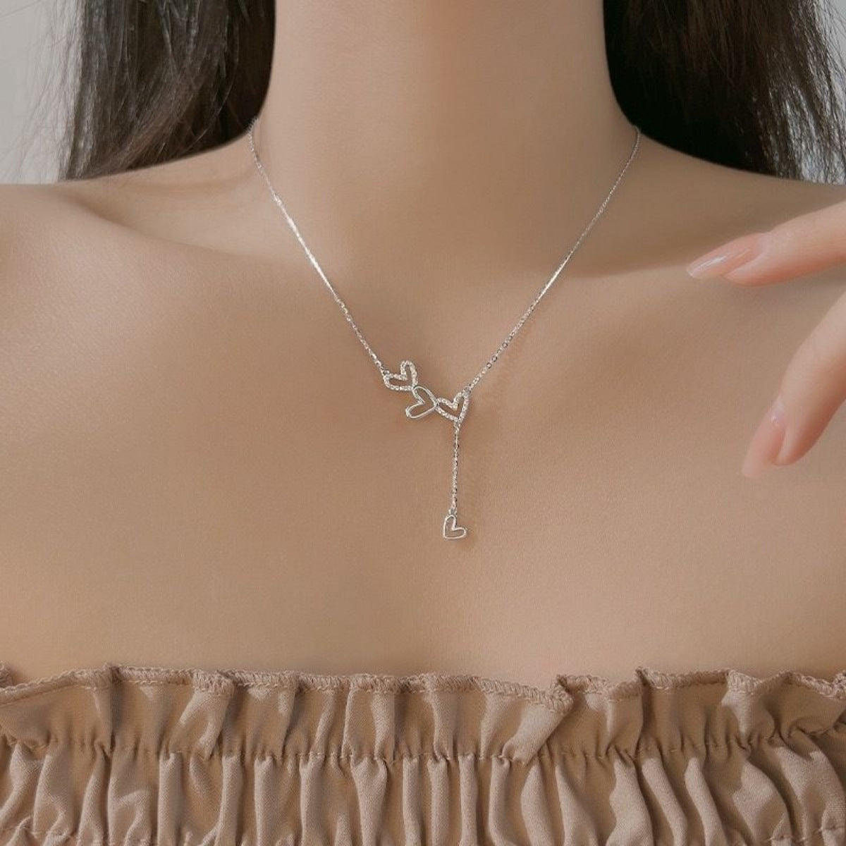 Sterling silver Y-necklace with delicate heart charms, resting on the collarbone.