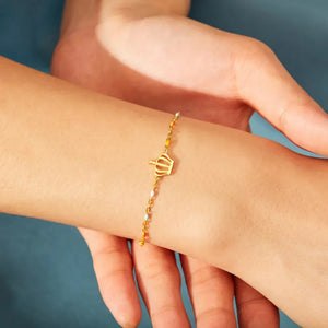 Gold bracelet with colorful enamel beads and a crown charm on a sterling silver chain.