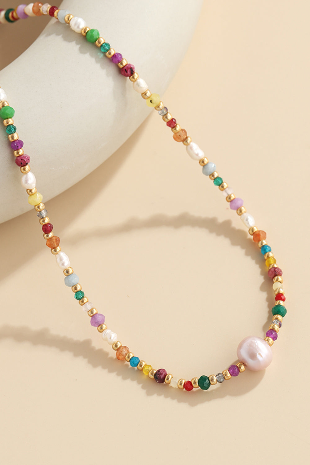 Multicolor beaded gemstone and pearl necklace with gold accents and a large pink pearl.
