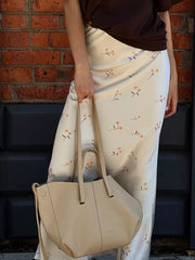 Satin floral print midi skirt with a bias cut and a beige tote bag.