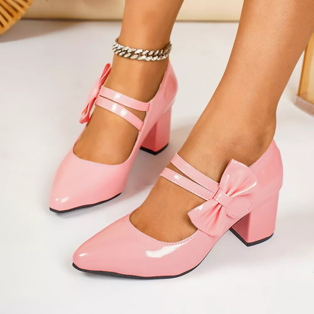 Pink patent block heel pumps with double ankle straps and bow detail.