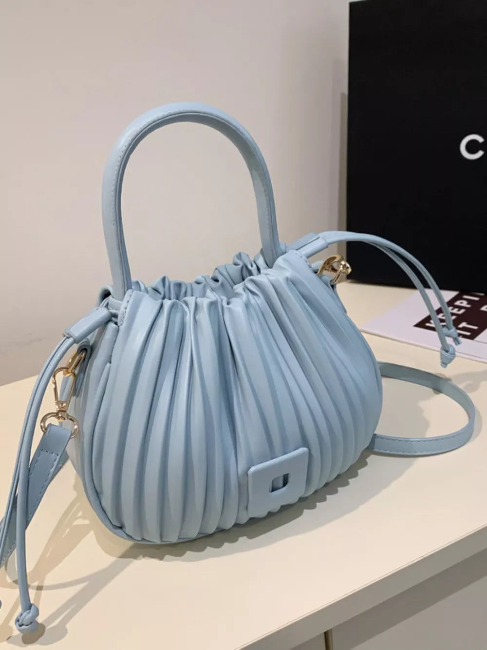 Blue pleated bucket bag with drawstring closure and top handle