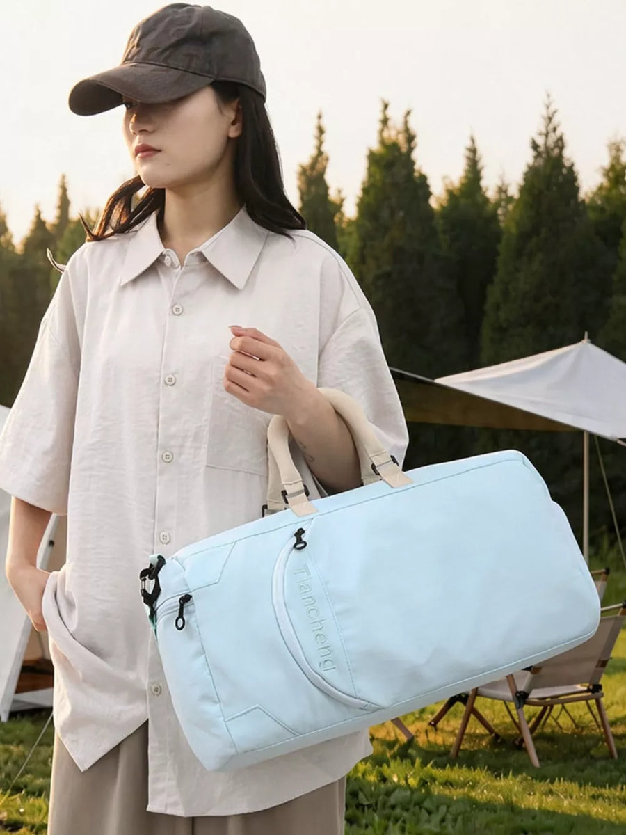 Light blue duffel bag with tan straps and embroidered logo, held by a woman in a beige shirt and cap.