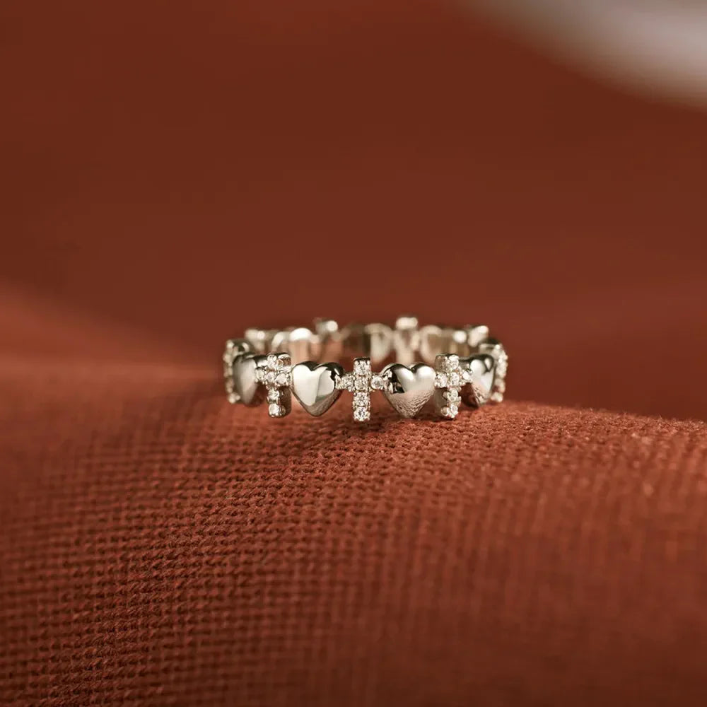 Sterling silver band ring with alternating heart and cross charms, accented with small stones.