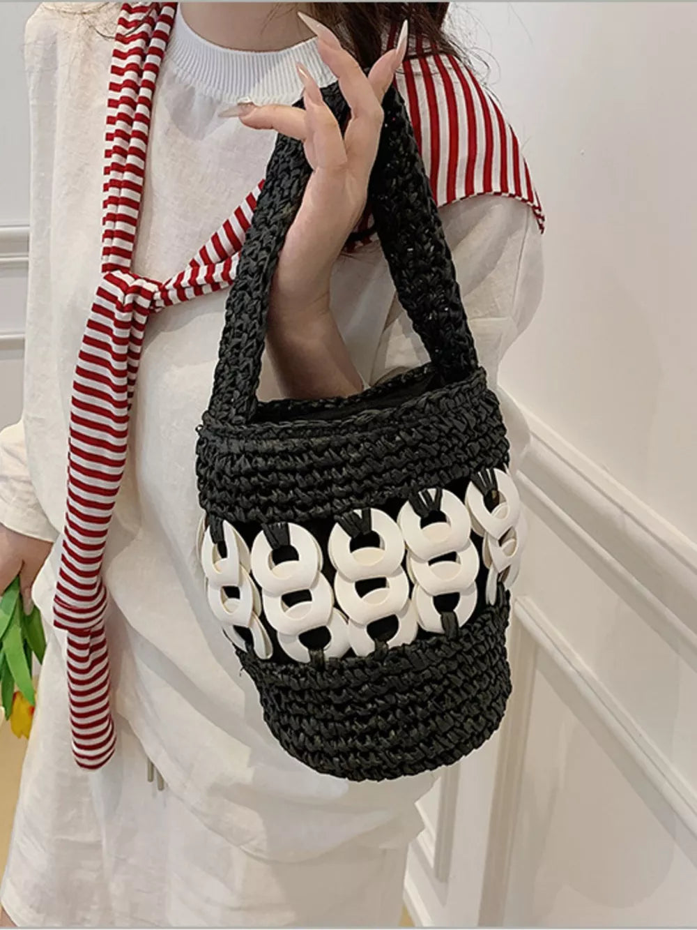 Black woven straw bucket tote with white ring detail and red striped scarf.