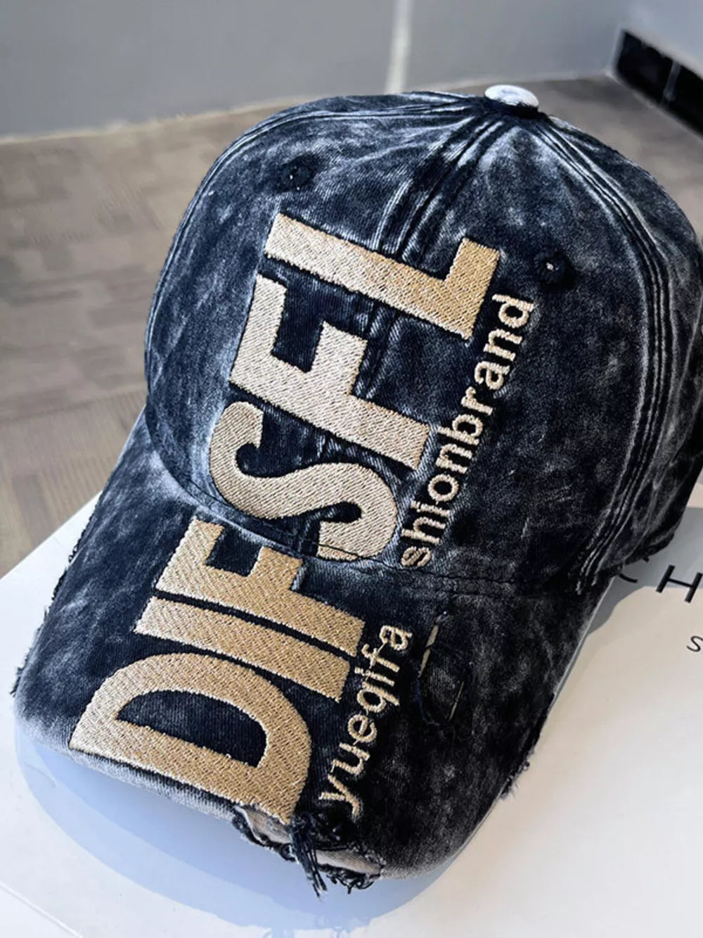 Distressed black baseball cap with gold embroidered text and frayed details.