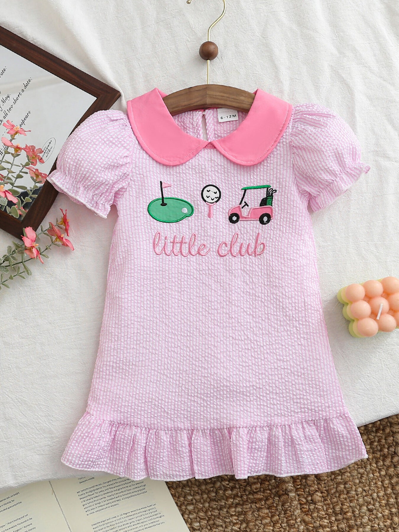 Pink seersucker baby dress with golf embroidery and ruffled hem.