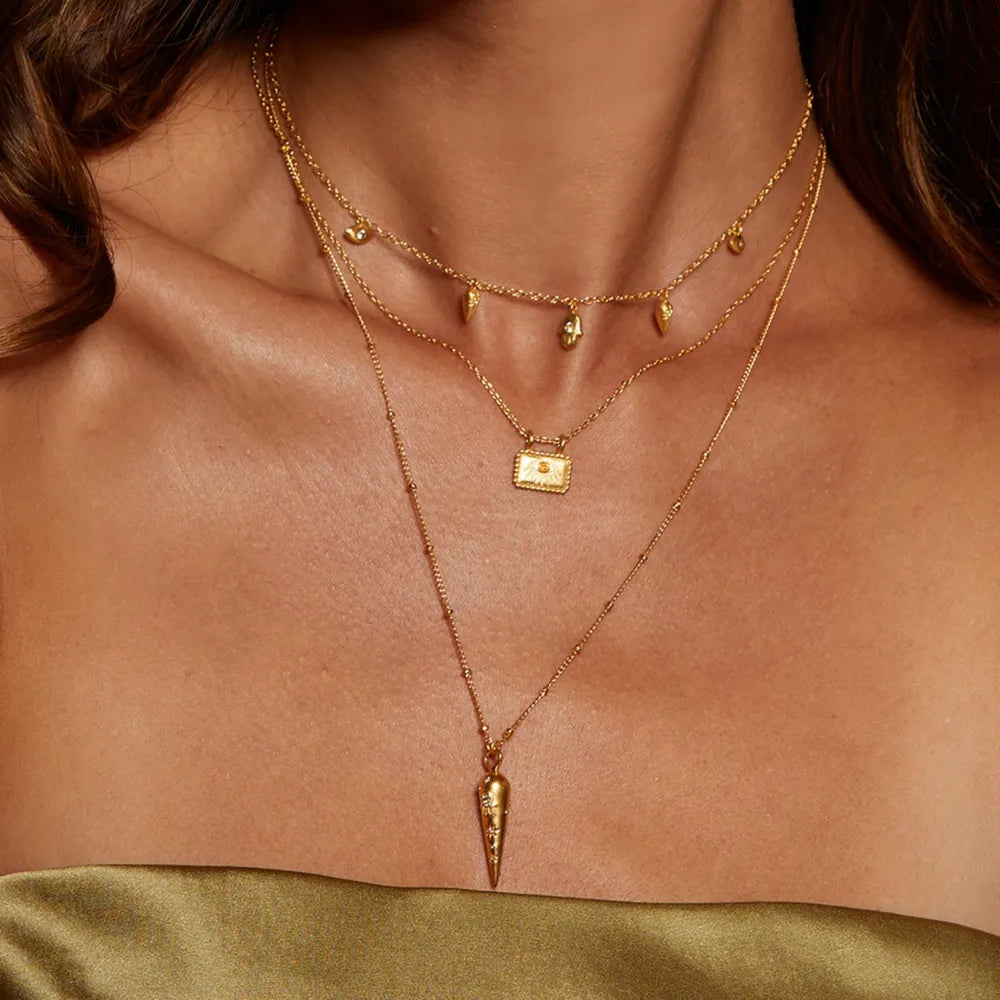 Layered gold necklaces with charms, a rectangular pendant, and a cone pendant.