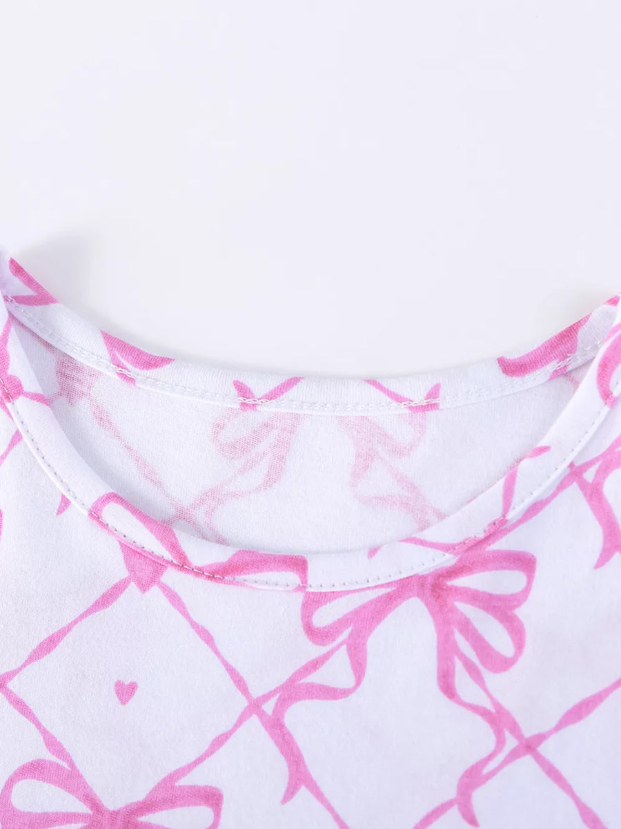 Baby dress with pink bow and heart print on white cotton fabric.