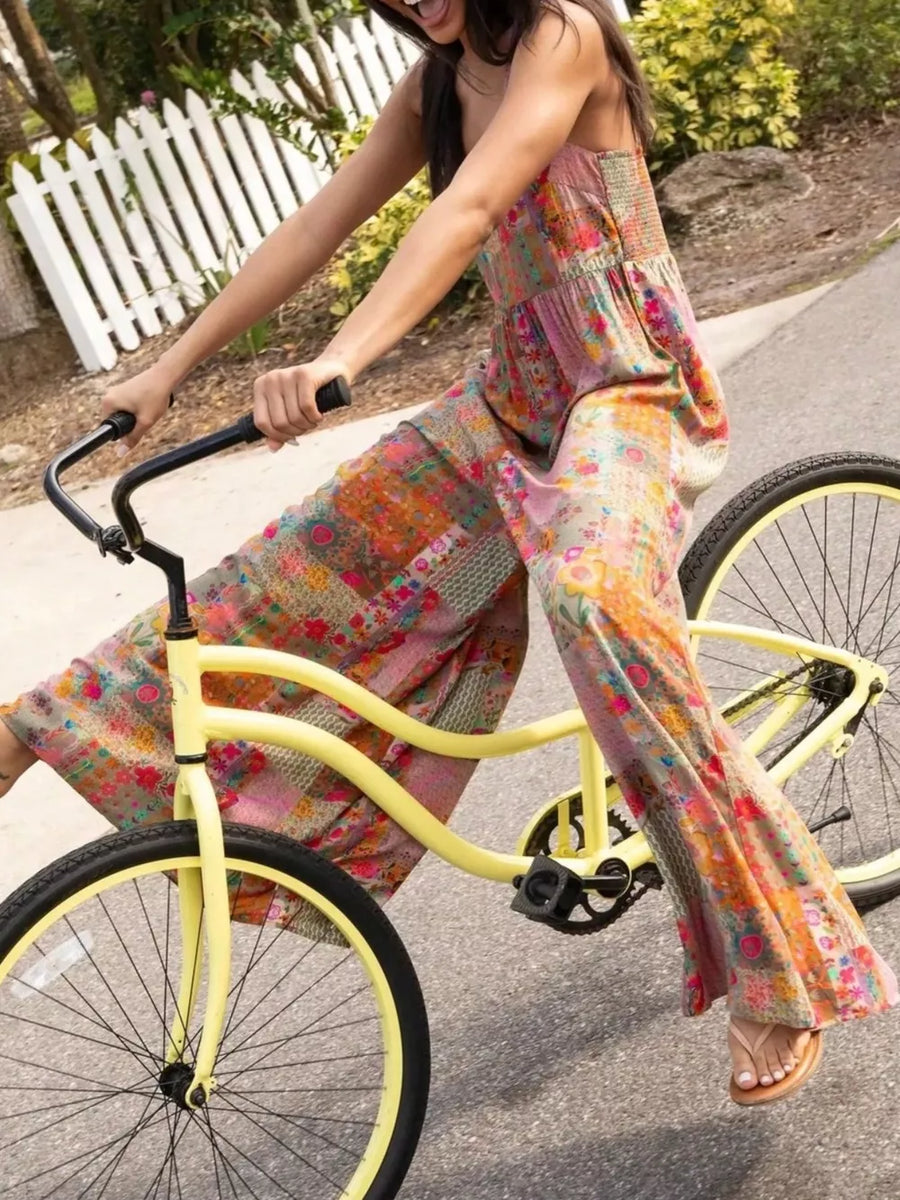 Vibrant patchwork wide-leg romper with smocked bodice and floral prints, worn by a woman cycling.