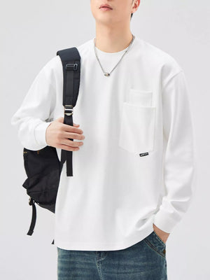 White long-sleeve sweatshirt with chest pocket and crew neck, styled with jeans and backpack.
