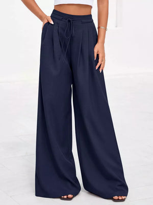 Dark blue high-waisted pleated wide-leg pants with pockets and drawstring waist.