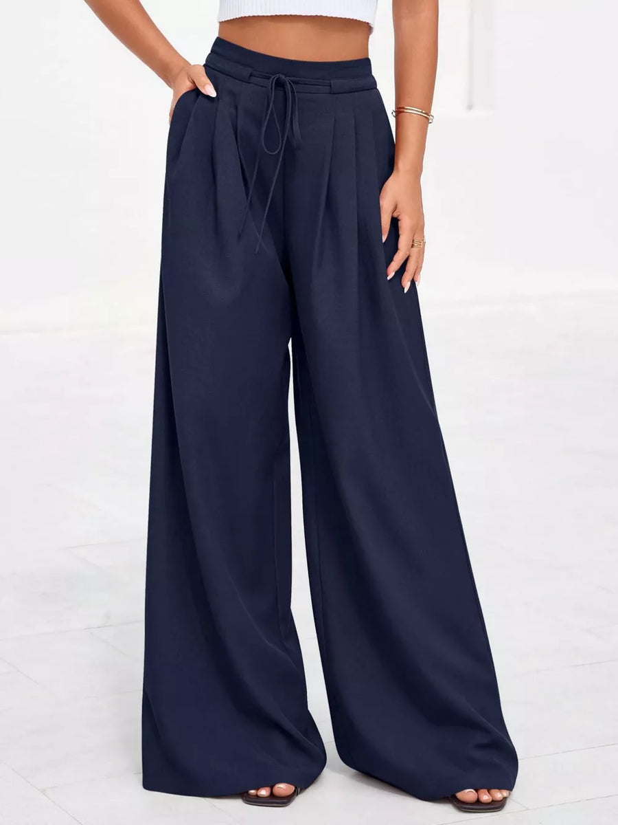 Dark blue high-waisted pleated wide-leg pants with pockets and drawstring waist.