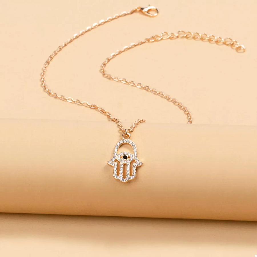 Gold evil eye Hamsa hand necklace with clear rhinestones and a black eye detail.