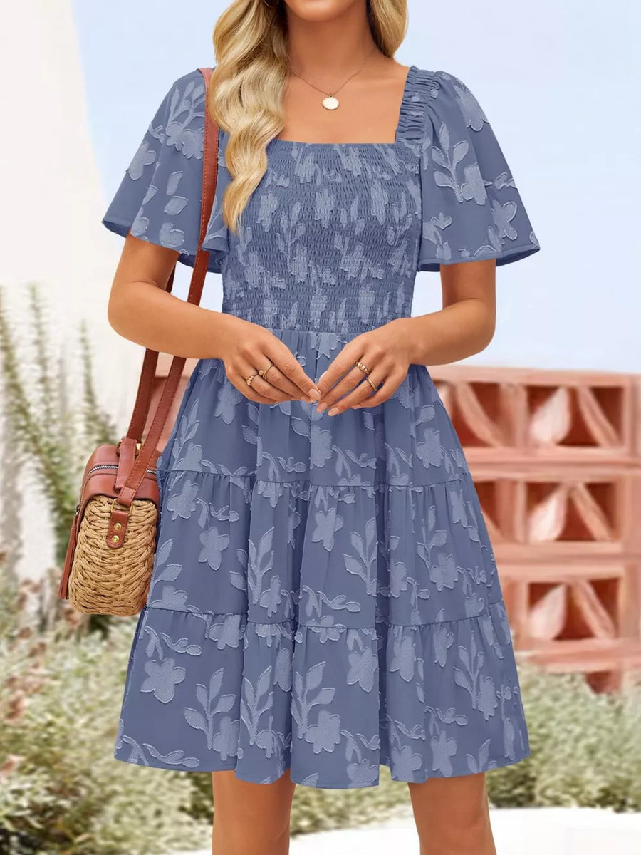 Dusty blue smocked mini dress with tiered skirt and floral texture.