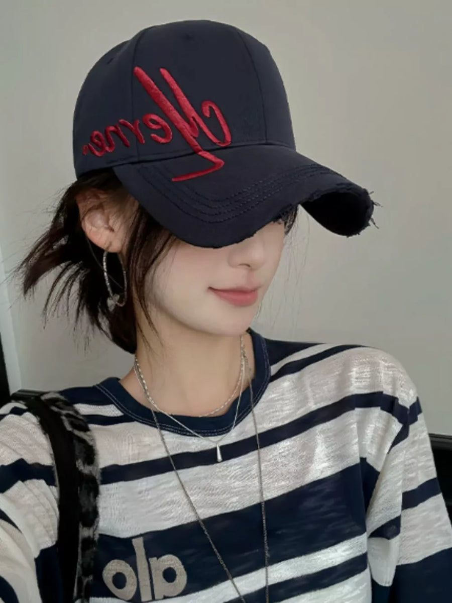 Navy baseball cap with red embroidered script and distressed brim, worn with a striped top.