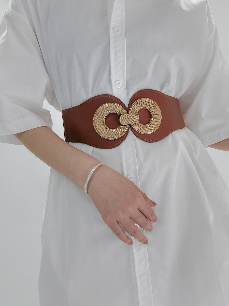 Caramel elastic belt with gold circular metalwork detail cinching a white shirt.