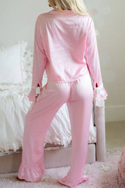 Blush pink silk pajama set with ruffle trim on collar, cuffs, and pant legs.