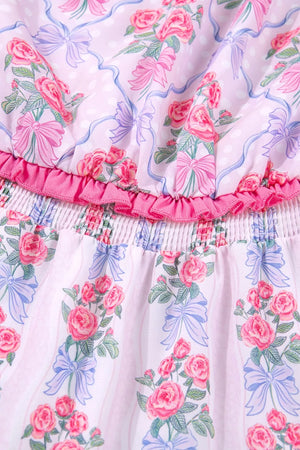 Floral tiered ruffle dress with pink roses and blue bows on a pink striped and polka dot background.