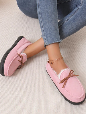Pink suede moccasin slippers with white faux fur lining and bow detail.
