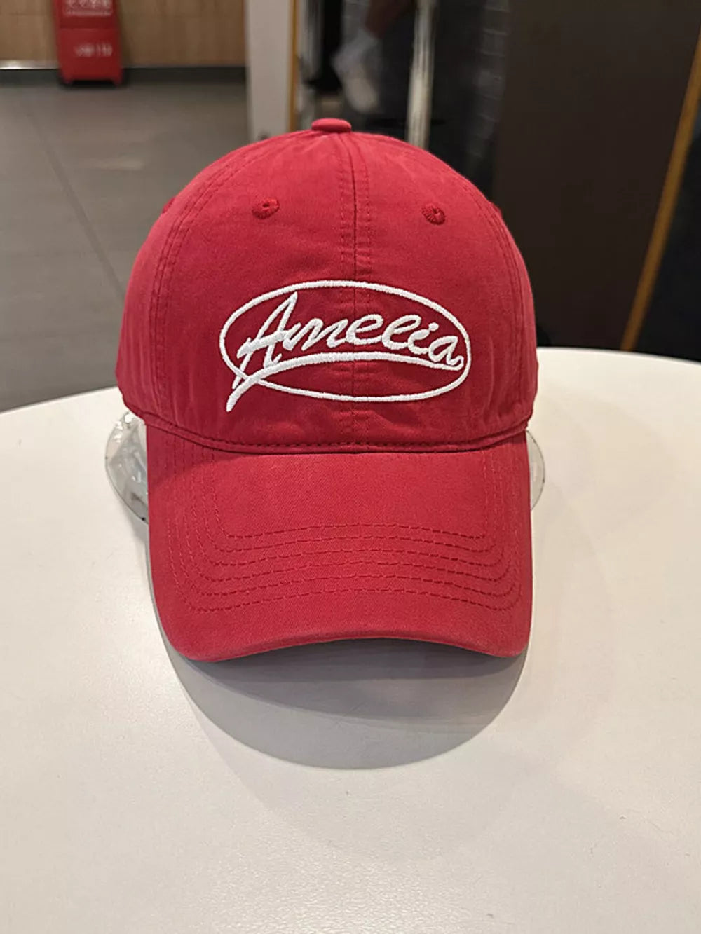 Red baseball cap with white Amelia embroidery and stitched brim