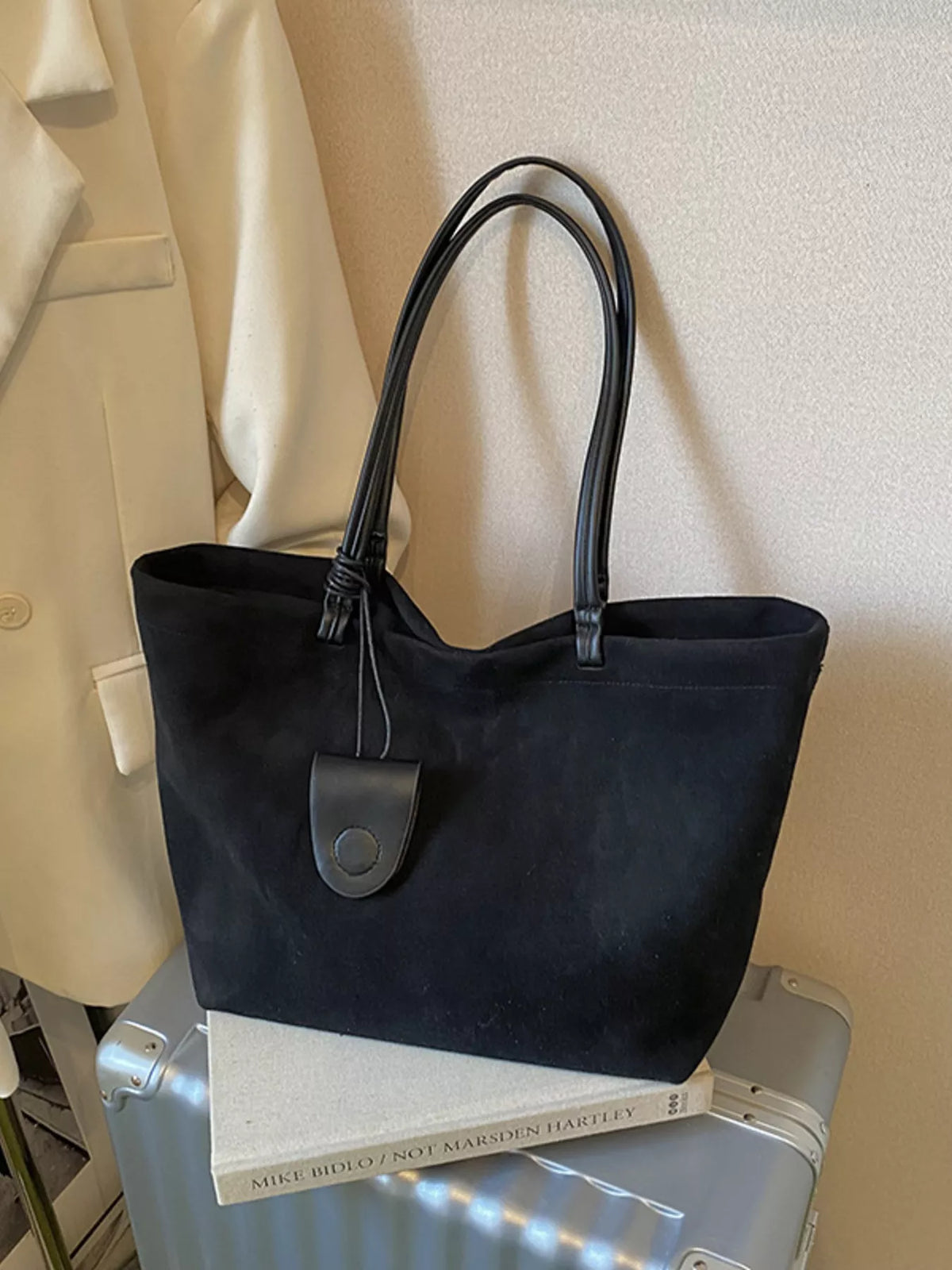 Large black suede tote bag with leather handles and a round charm detail.