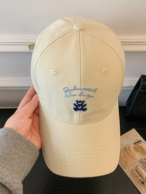 Cream baseball cap with blue embroidered teddy bear and text detail