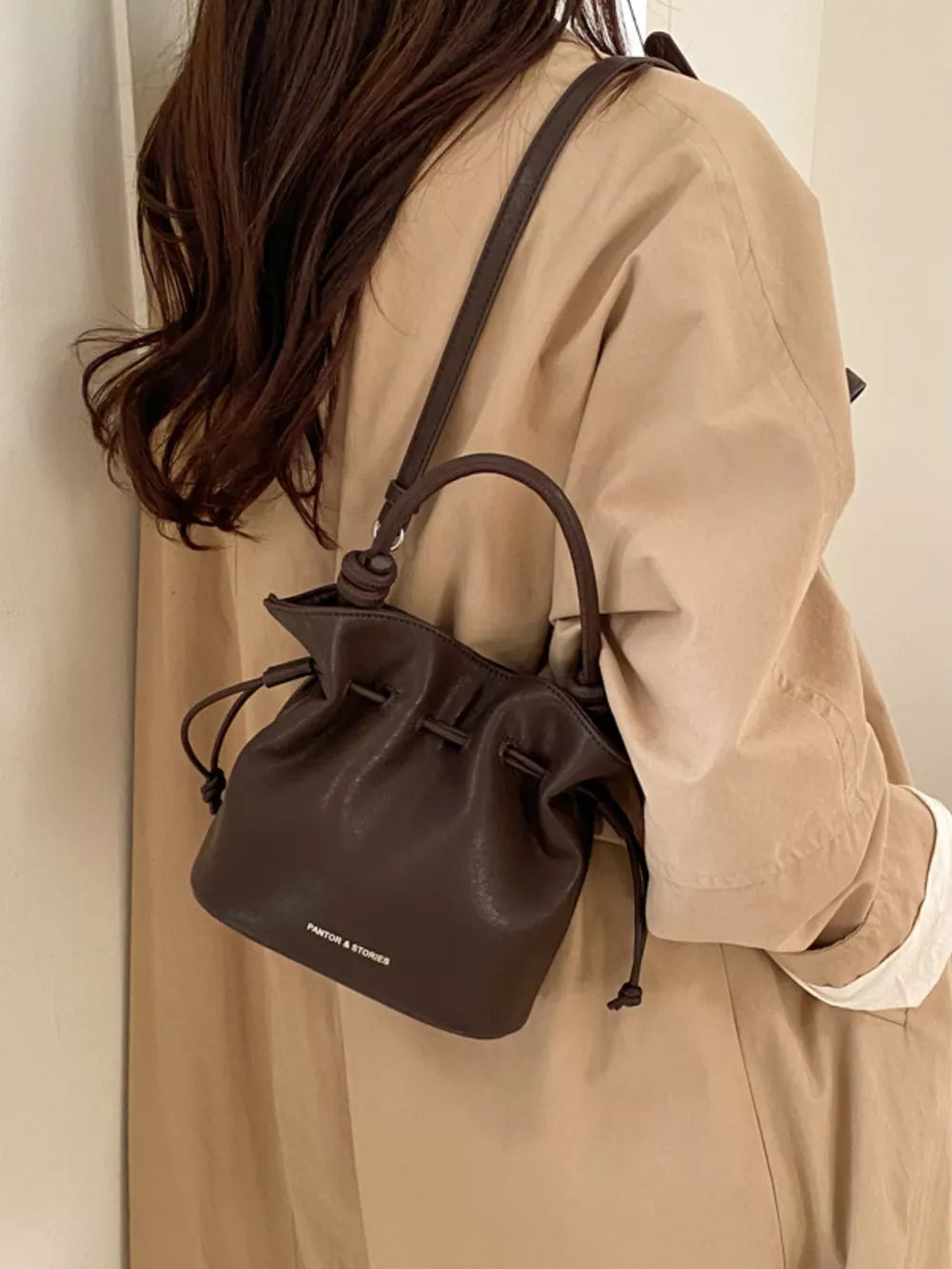 Brown pu leather cinch-top crossbody bag with drawstring detail and top handle.