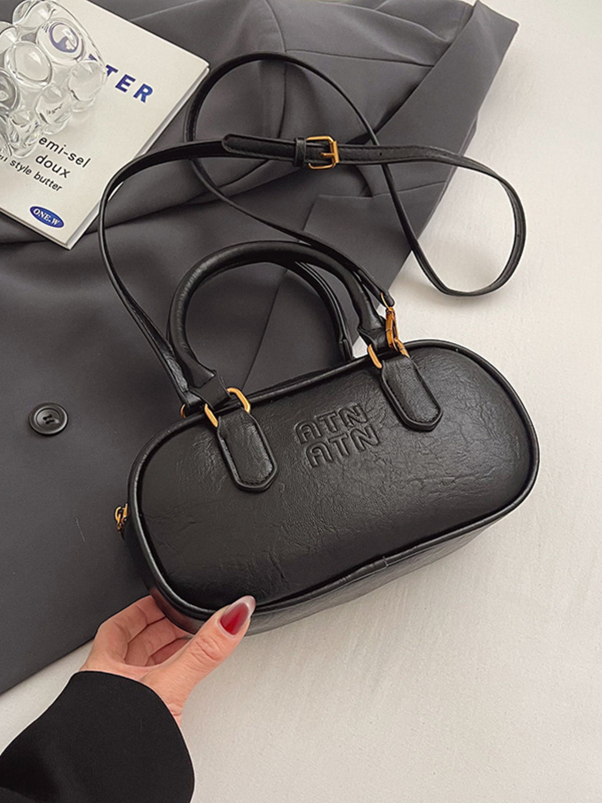 Black oval pu leather crossbody bag with embossed logo and adjustable strap