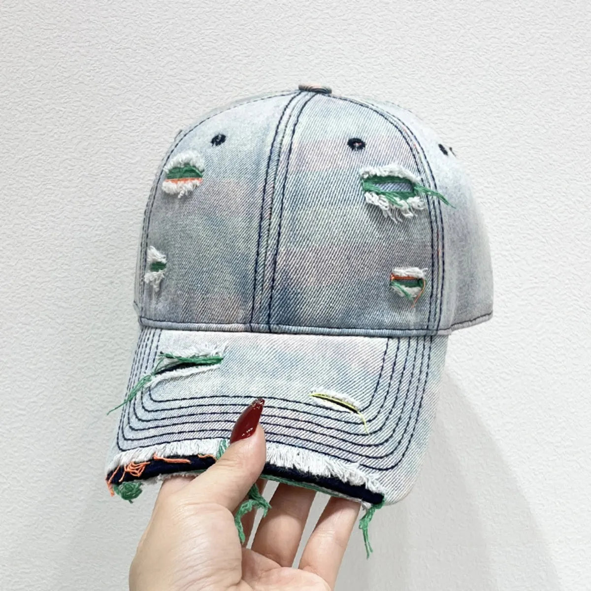 Light blue distressed denim baseball cap with fraying and green accents.