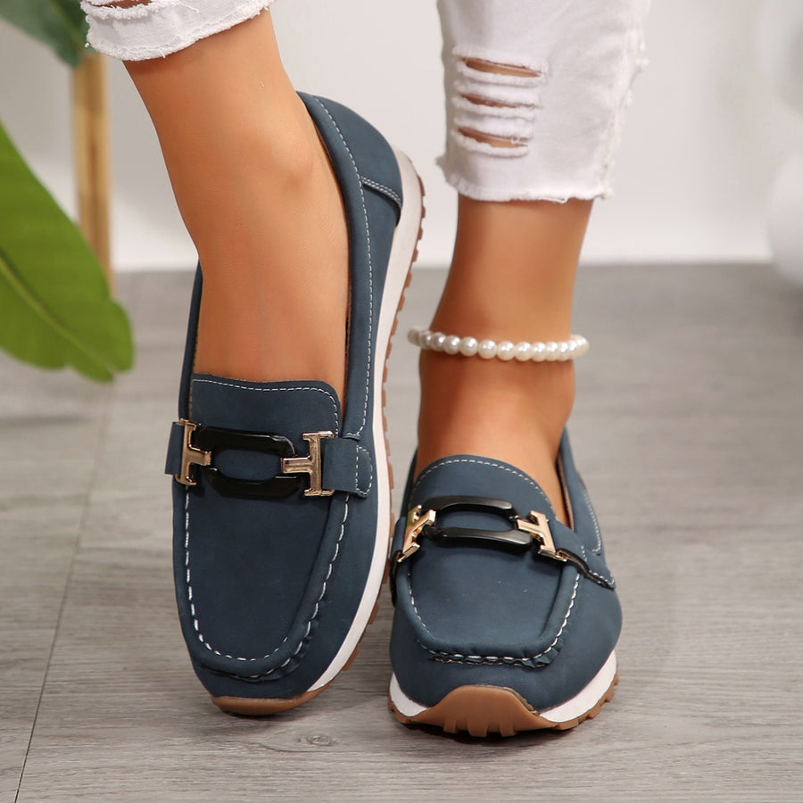 Dark blue slip-on loafers with gold buckle detail and contrast stitching.