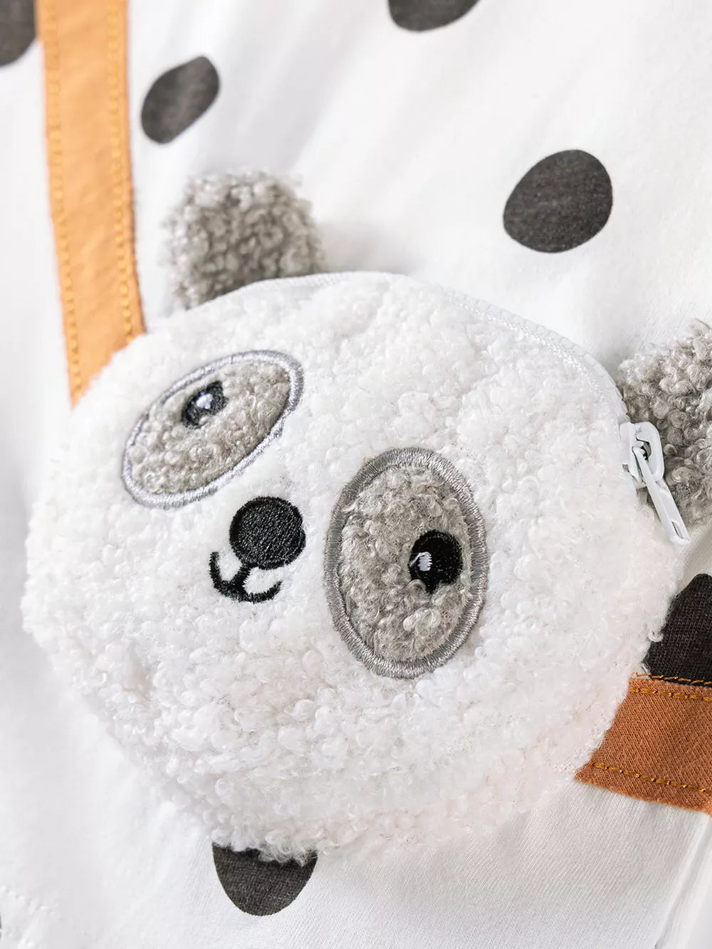 White baby outfit with black polka dots and a plush panda face detail.