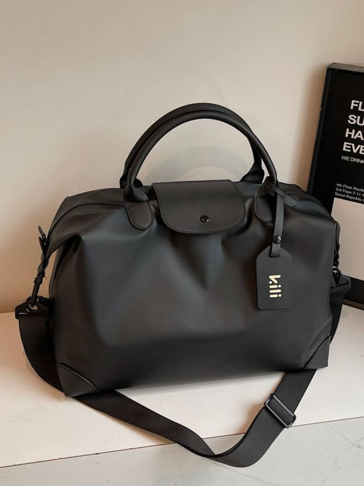 Black minimalist large travel duffel bag with detachable strap and luggage tag.