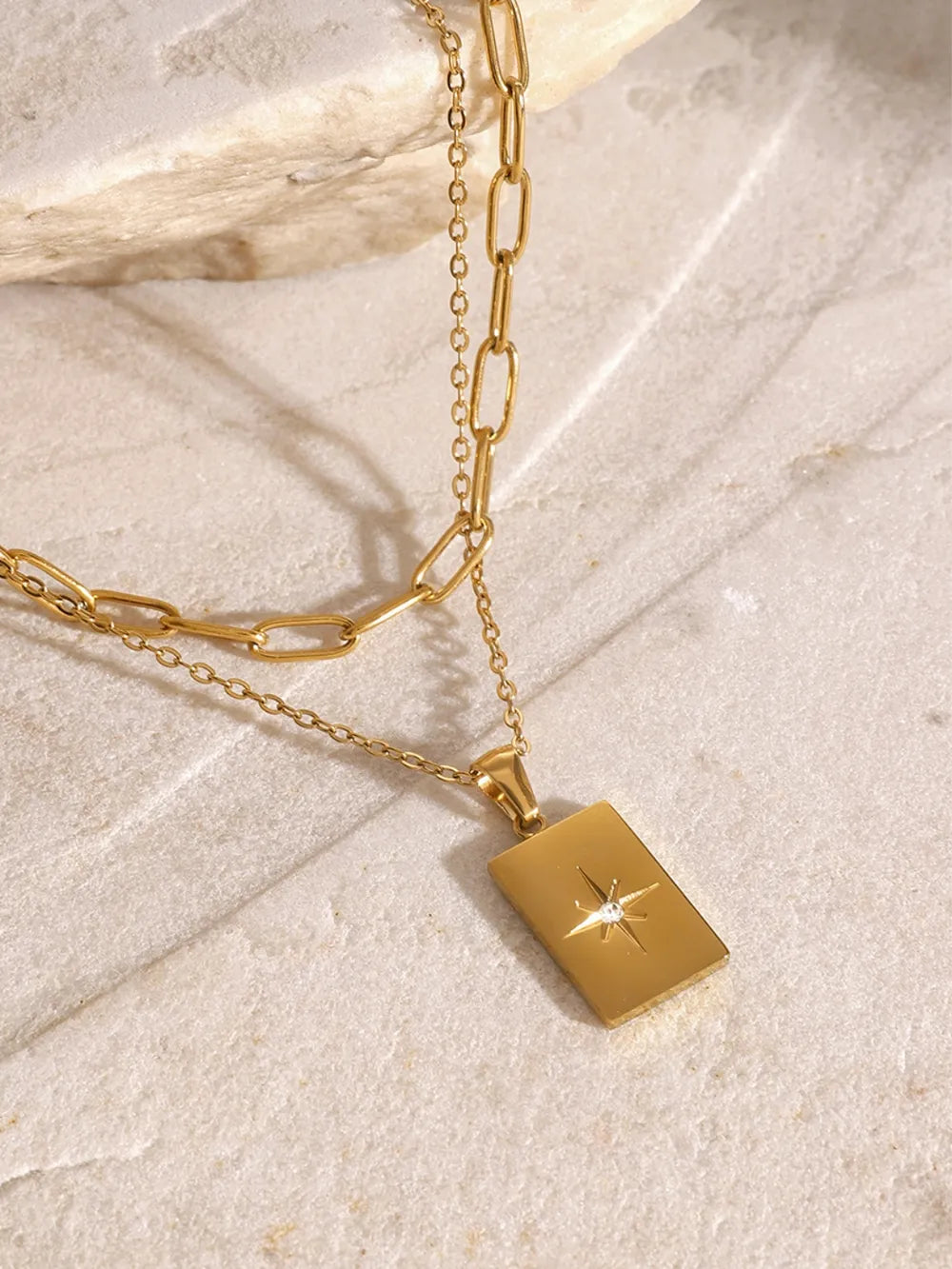 Gold layered chain necklace with celestial starburst pendant and crystal accent.