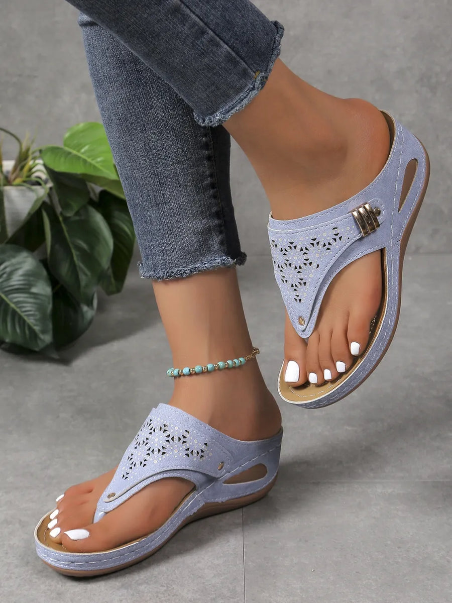 Dusty blue laser-cut thong sandals with decorative buckle detail and wedge heel.