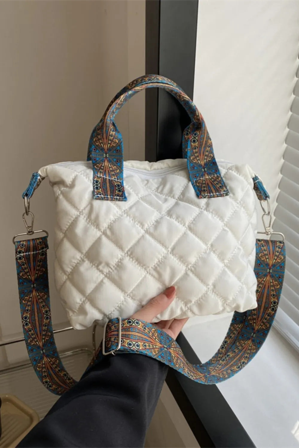 White quilted satchel bag with a patterned strap and top handles.
