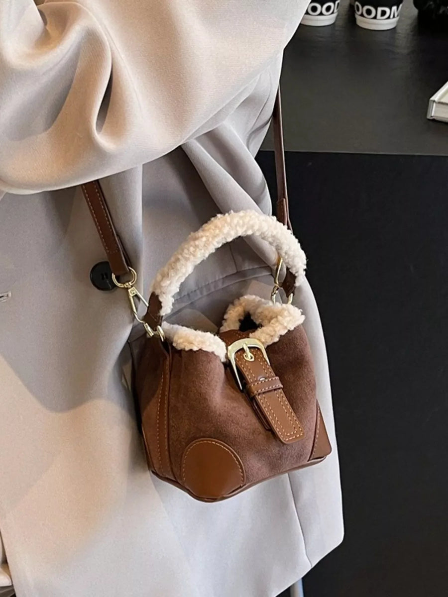 Brown suede bucket bag with fuzzy trim and buckle detail, worn crossbody.