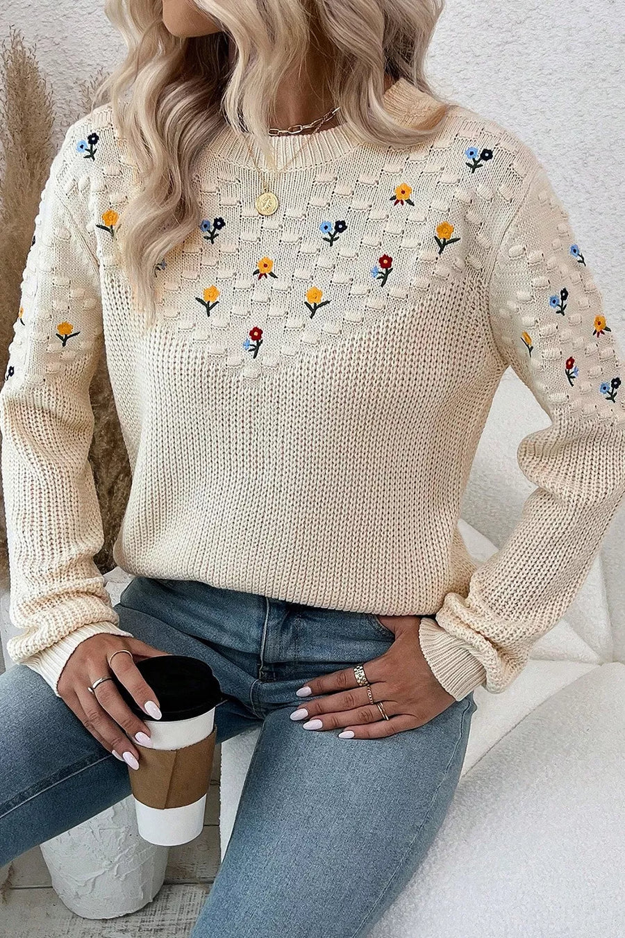 Beige embroidered round-neck sweater with dropped shoulders and a textured knit pattern.