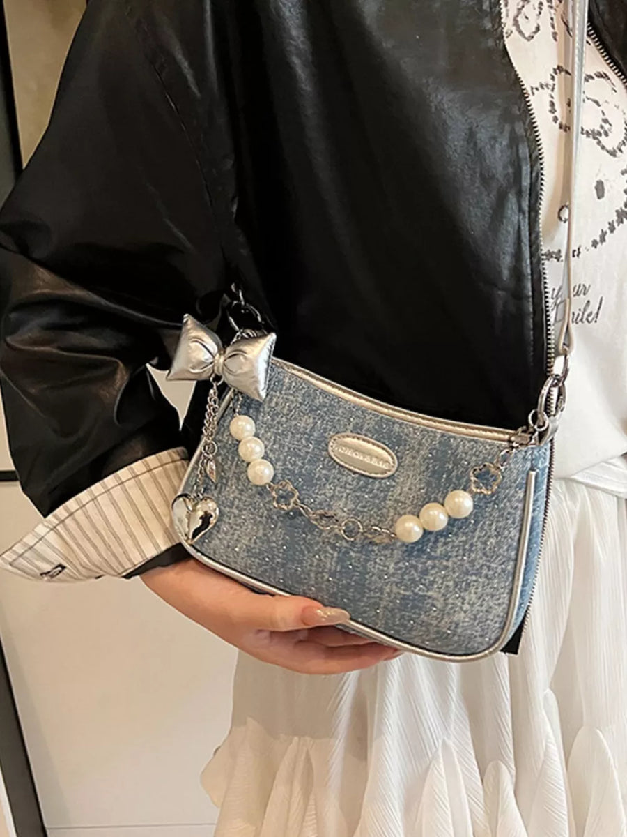 Light denim shoulder bag with pearl chain, heart charm, and bow detail.