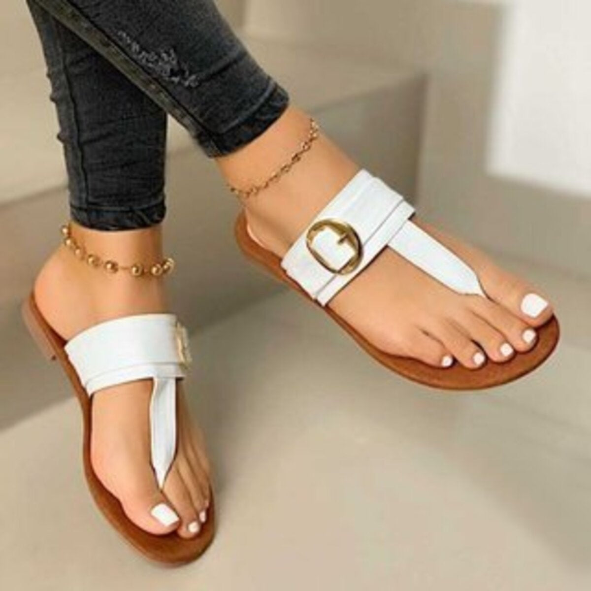 White toe-post sandals with gold buckle detail and white pedicure.