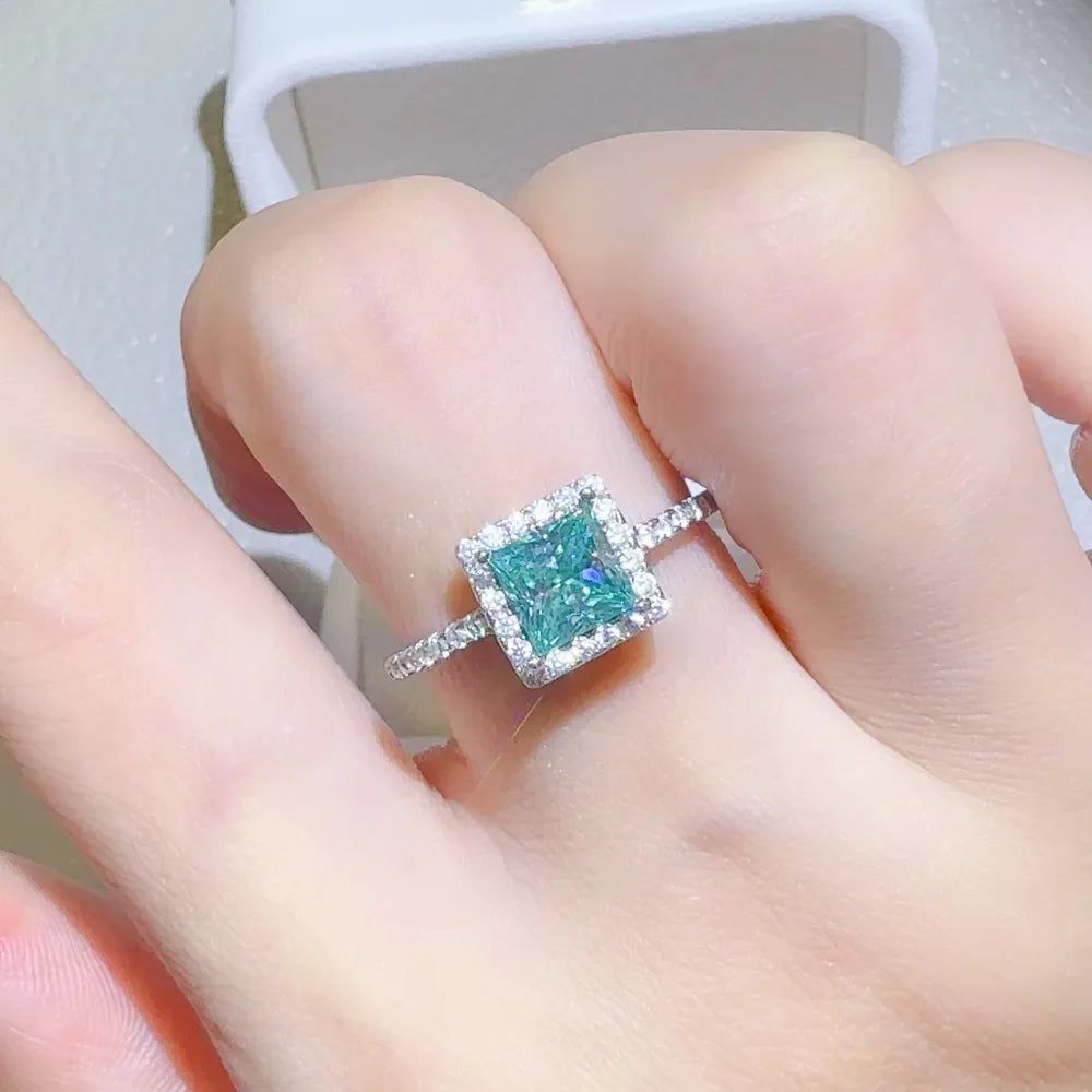 Radiant square halo moissanite ring in silver with a bright teal center stone.